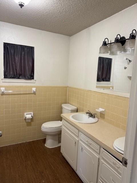 full bath featuring a textured ceiling, toilet, wood finished floors, a sink, and double vanity