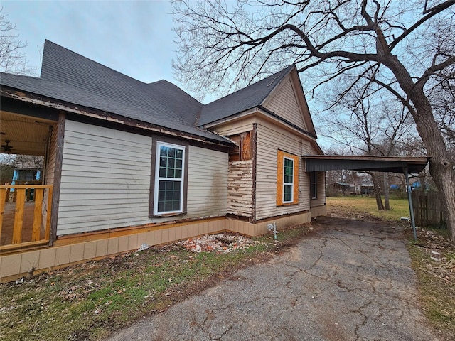 view of home's exterior with aphalt driveway, a carport, and roof with shingles