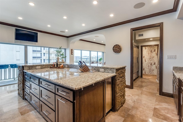 kitchen with light stone counters, a center island, crown molding, and dark brown cabinets