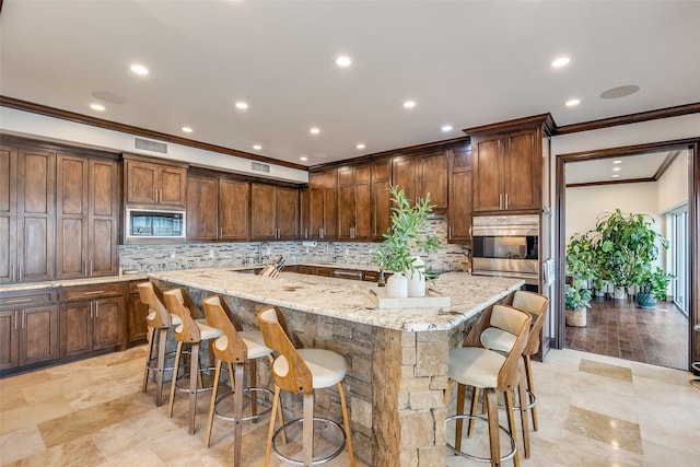 kitchen featuring black microwave, a large island with sink, a kitchen bar, and light stone countertops