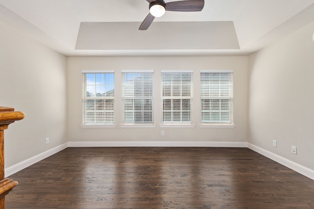 unfurnished room featuring dark wood-style flooring, a raised ceiling, ceiling fan, and baseboards