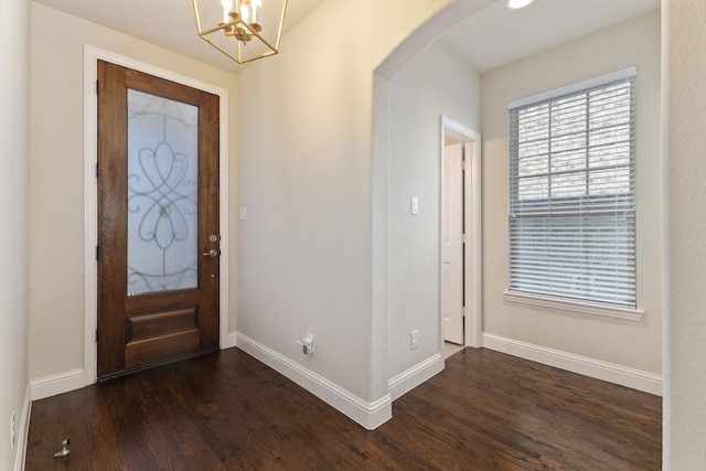 entryway with an inviting chandelier, baseboards, arched walkways, and dark wood finished floors