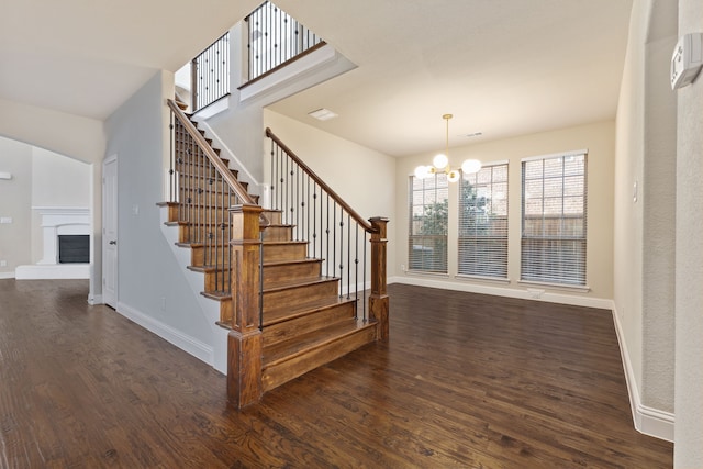 stairs featuring a fireplace with raised hearth, baseboards, wood finished floors, and a chandelier