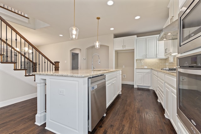 kitchen with light stone counters, a sink, white cabinets, appliances with stainless steel finishes, and a center island with sink