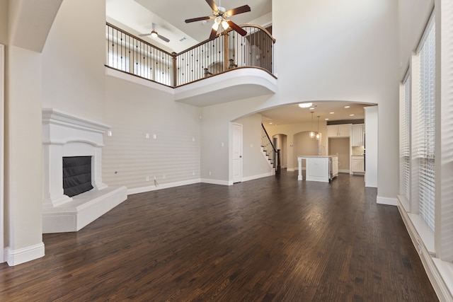 unfurnished living room featuring arched walkways, dark wood-style flooring, a fireplace with raised hearth, and baseboards