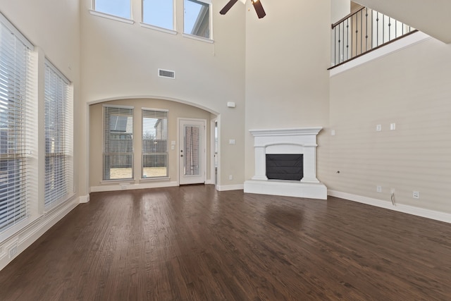 unfurnished living room featuring a fireplace with raised hearth, dark wood-type flooring, visible vents, a ceiling fan, and baseboards