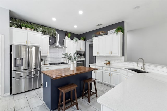 kitchen featuring stainless steel appliances, a sink, white cabinets, wooden counters, and wall chimney exhaust hood