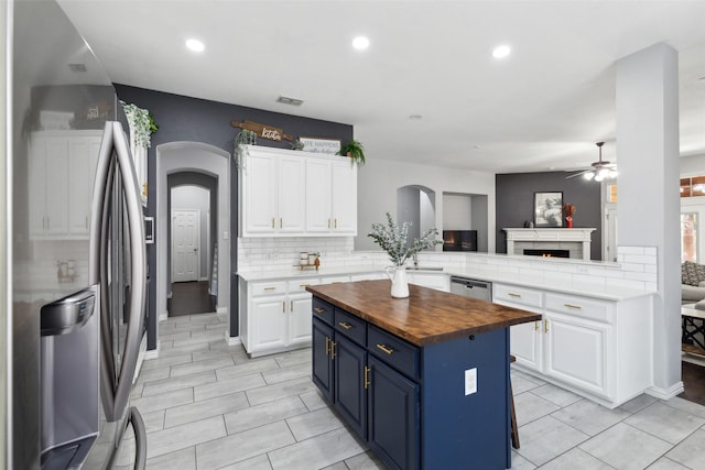 kitchen with butcher block countertops, arched walkways, white cabinetry, and a peninsula