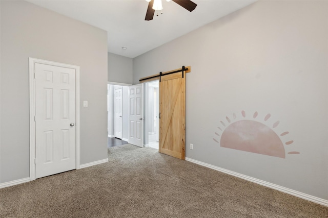 unfurnished bedroom featuring carpet floors, a barn door, a ceiling fan, and baseboards