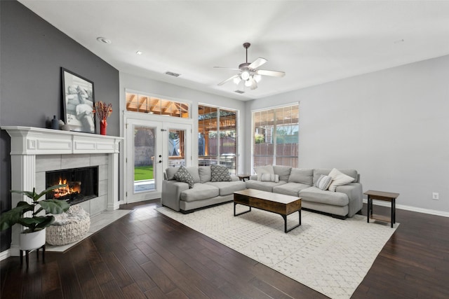 living area featuring dark wood finished floors, visible vents, a tiled fireplace, a ceiling fan, and baseboards