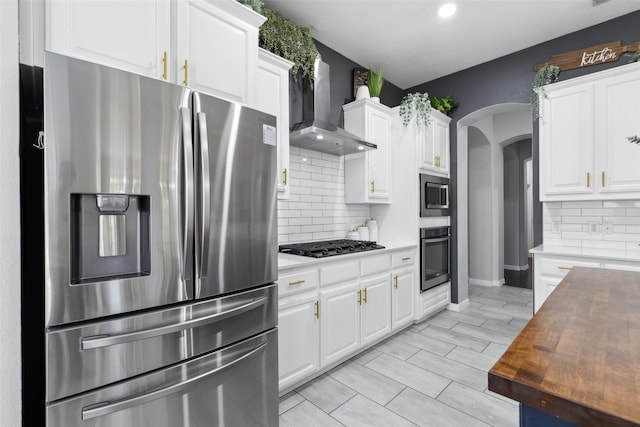 kitchen featuring wall chimney exhaust hood, appliances with stainless steel finishes, and white cabinets