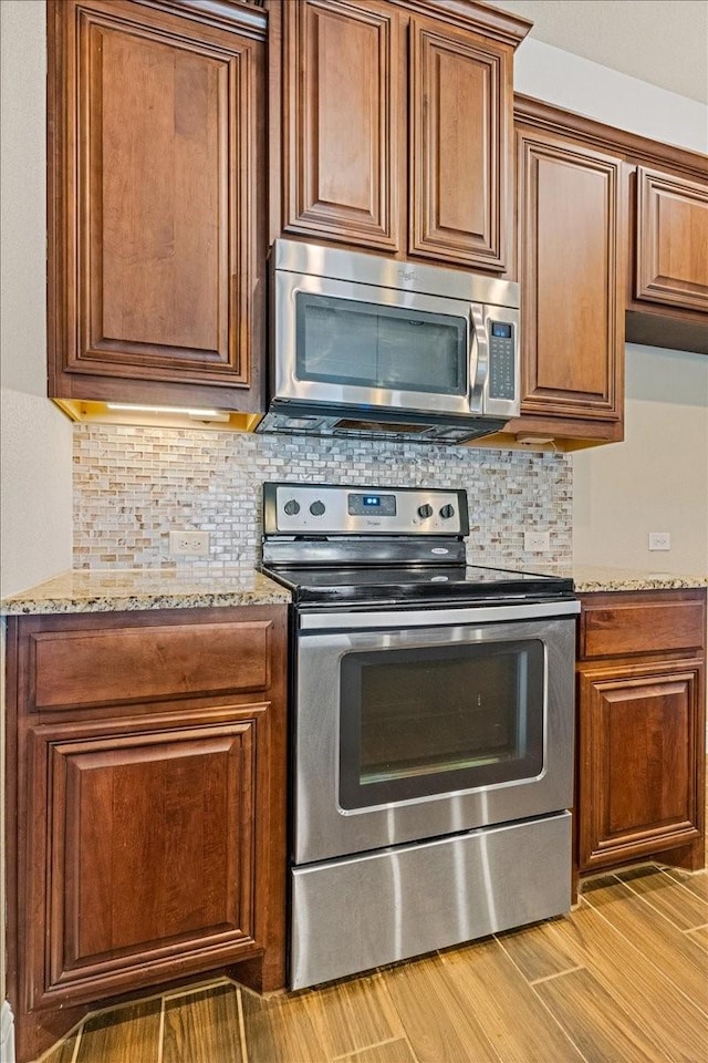 kitchen with brown cabinets, light wood finished floors, stainless steel appliances, decorative backsplash, and light stone countertops