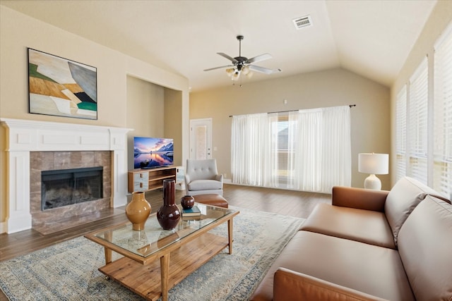 living area with visible vents, vaulted ceiling, wood finished floors, and a tile fireplace