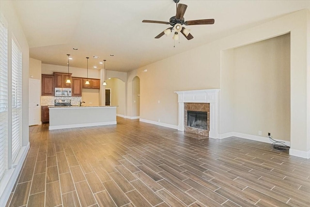 unfurnished living room featuring baseboards, arched walkways, a ceiling fan, wood tiled floor, and a fireplace