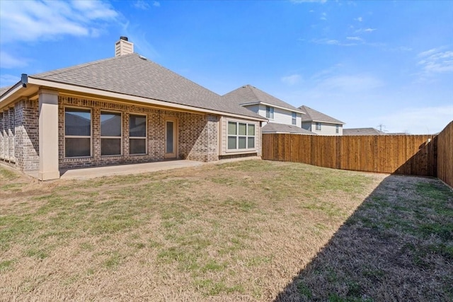 back of house with brick siding, a chimney, a lawn, a patio area, and a fenced backyard