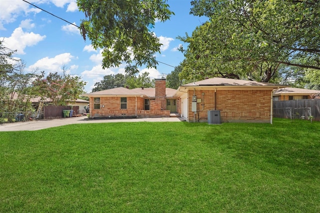 back of house featuring brick siding, a chimney, a lawn, central AC, and fence