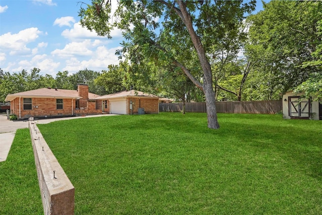 view of yard featuring a storage unit, concrete driveway, an attached garage, fence, and an outdoor structure