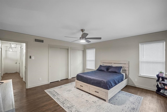 bedroom with baseboards, visible vents, a ceiling fan, dark wood finished floors, and two closets