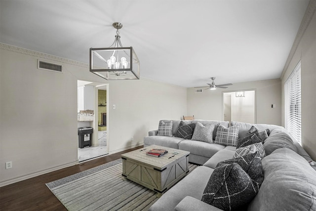 living area with baseboards, visible vents, dark wood-style flooring, and ceiling fan with notable chandelier