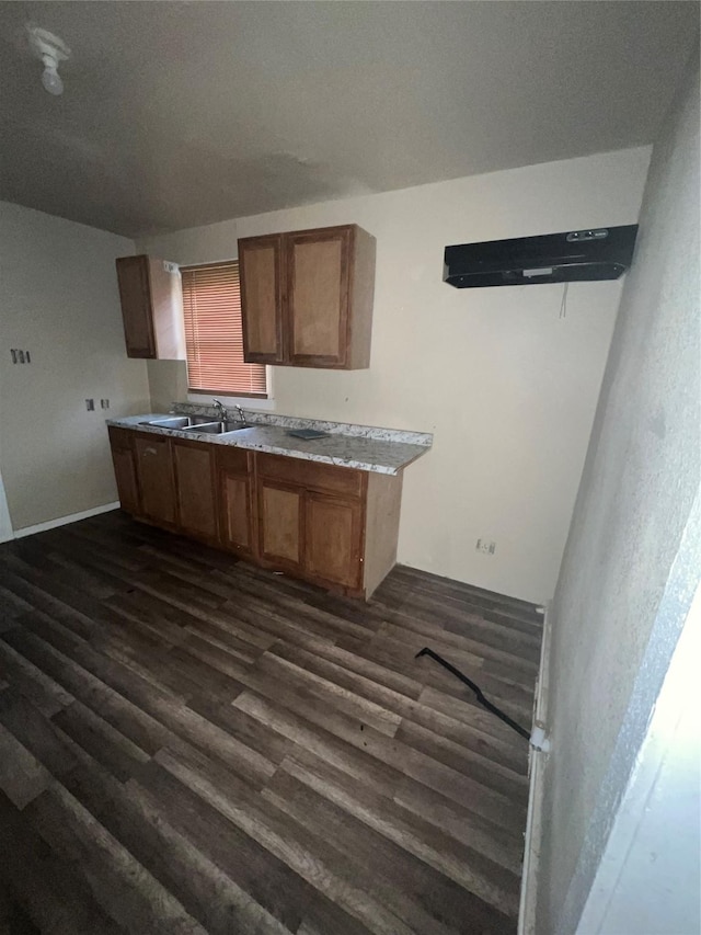 kitchen with brown cabinetry, dark wood-style flooring, light countertops, and a sink