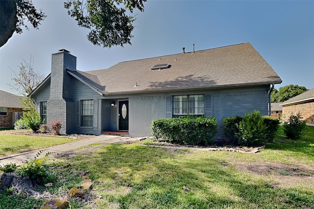 view of front of home with a shingled roof, a chimney, a front lawn, and brick siding