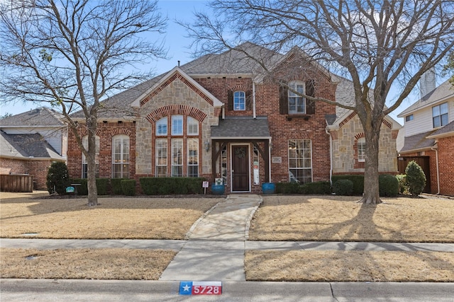 view of front of house featuring stone siding, a shingled roof, and brick siding