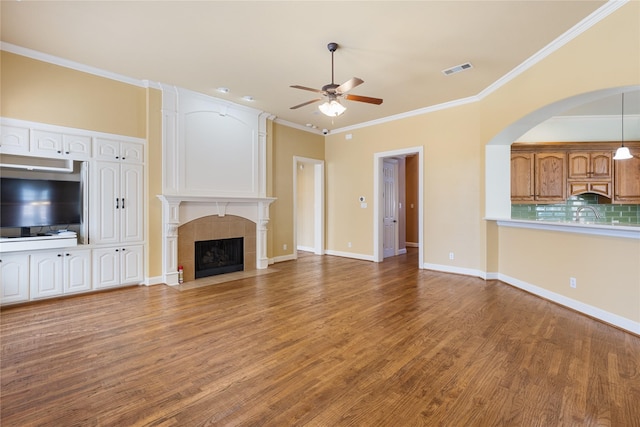 unfurnished living room with crown molding, visible vents, a tiled fireplace, and wood finished floors