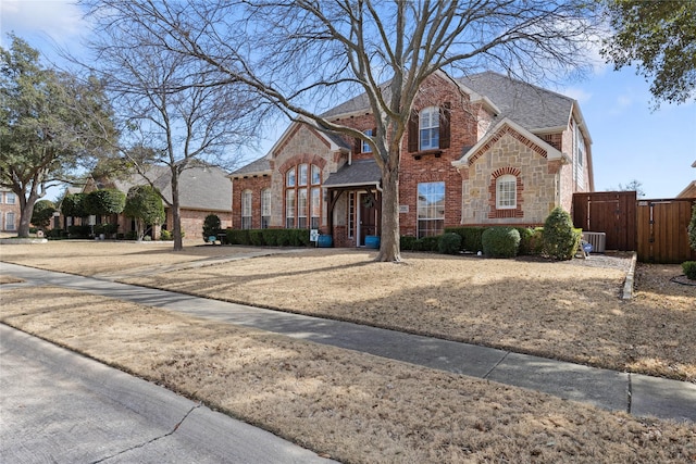 view of front of property featuring stone siding, roof with shingles, a gate, cooling unit, and brick siding