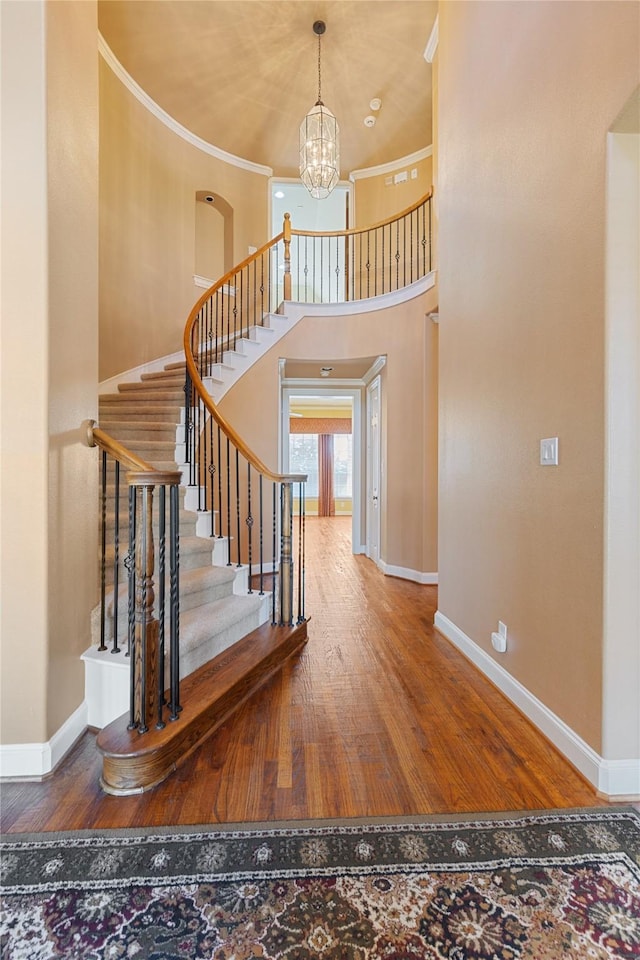 staircase featuring a chandelier, a towering ceiling, baseboards, and wood finished floors