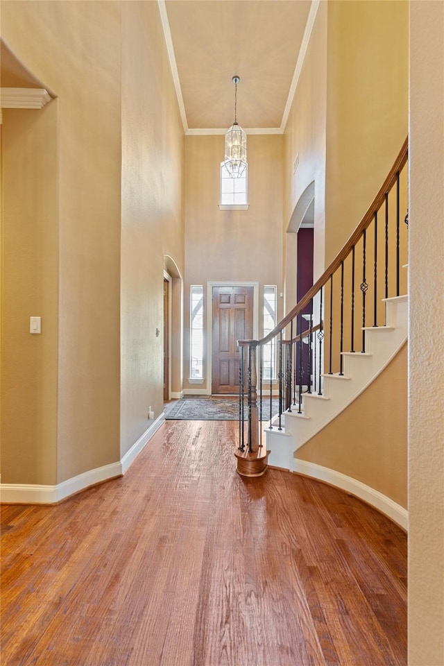 foyer entrance featuring baseboards, ornamental molding, wood finished floors, stairs, and a notable chandelier