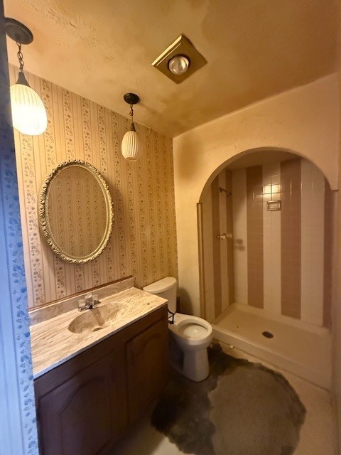 bathroom featuring toilet, a stall shower, vanity, and wallpapered walls