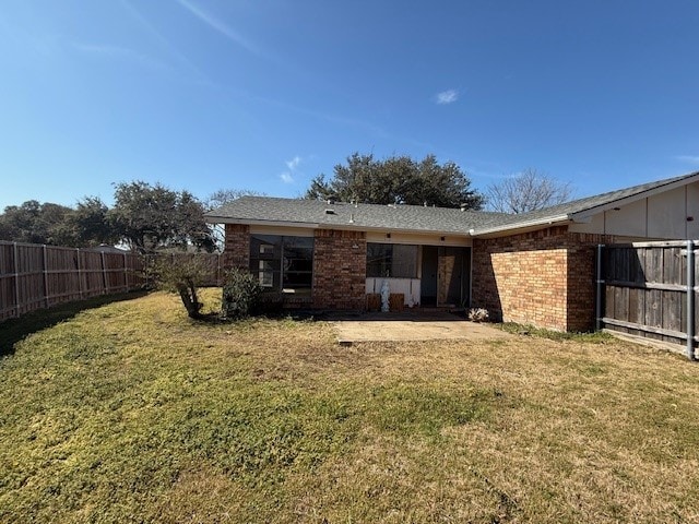 rear view of house featuring a fenced backyard, a lawn, and brick siding