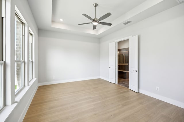 unfurnished bedroom featuring light wood-style floors, visible vents, multiple windows, and a tray ceiling