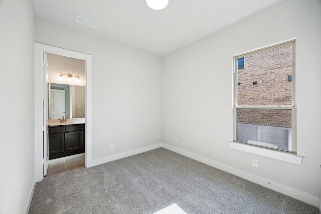 unfurnished bedroom featuring light colored carpet, visible vents, a sink, ensuite bath, and baseboards