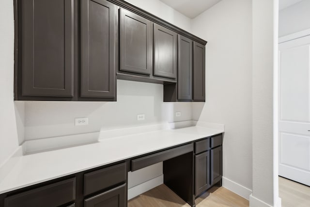 kitchen featuring baseboards, light countertops, dark brown cabinets, light wood-style floors, and built in desk