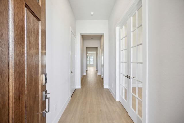 hallway featuring french doors, baseboards, and light wood finished floors