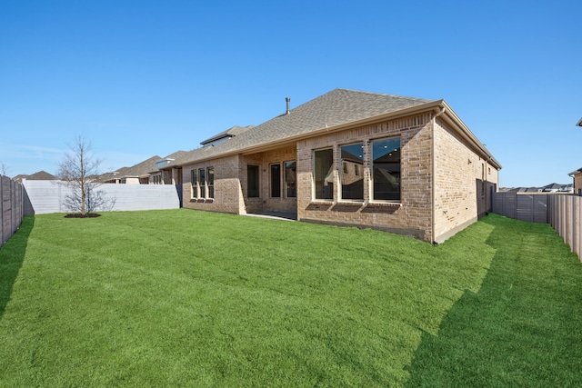 rear view of property featuring roof with shingles, a fenced backyard, brick siding, and a lawn