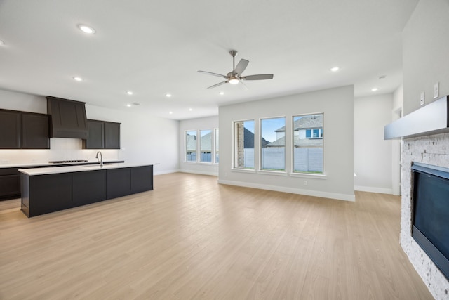 kitchen featuring a center island with sink, open floor plan, custom exhaust hood, light countertops, and a fireplace