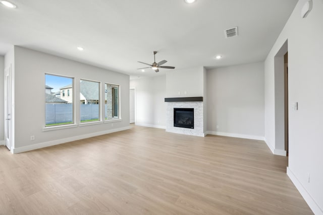 unfurnished living room with ceiling fan, a stone fireplace, visible vents, baseboards, and light wood-style floors