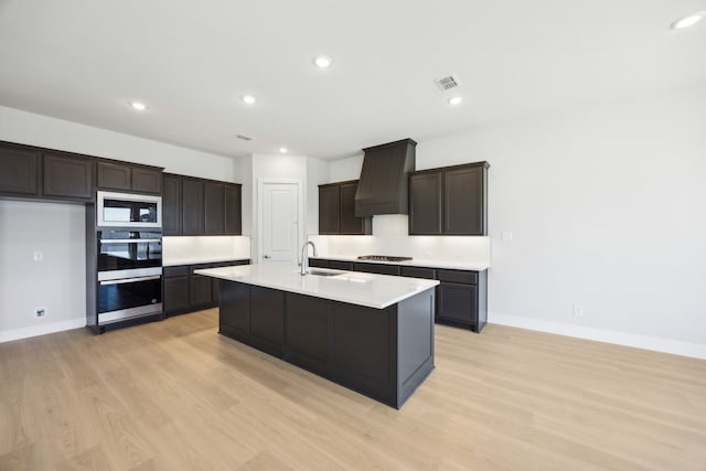 kitchen with a center island with sink, gas stovetop, custom exhaust hood, light countertops, and built in microwave