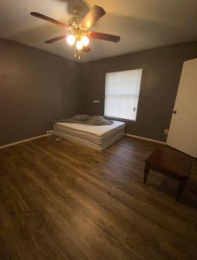 unfurnished bedroom featuring ceiling fan, dark wood-type flooring, and baseboards