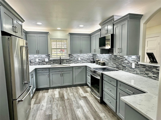 kitchen featuring light stone counters, gray cabinets, light wood-style flooring, appliances with stainless steel finishes, and a sink