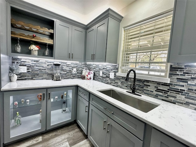 kitchen with light stone counters, gray cabinets, a sink, and backsplash