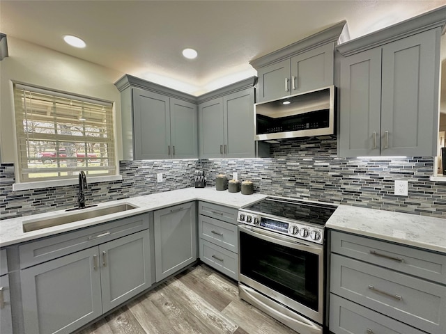 kitchen with stainless steel appliances, light stone counters, a sink, and gray cabinetry