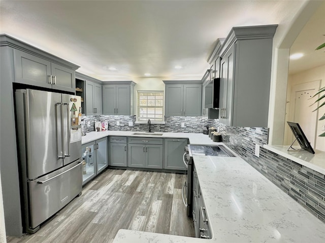 kitchen featuring light stone counters, a sink, appliances with stainless steel finishes, gray cabinets, and tasteful backsplash