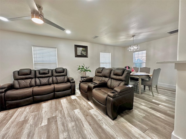 living area with visible vents, light wood-style flooring, baseboards, and ceiling fan with notable chandelier