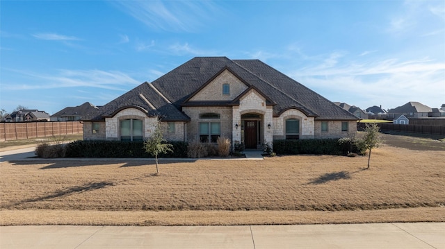 french provincial home with stone siding, fence, and roof with shingles