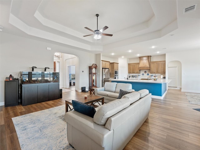 living area featuring arched walkways, a tray ceiling, light wood-style flooring, and visible vents