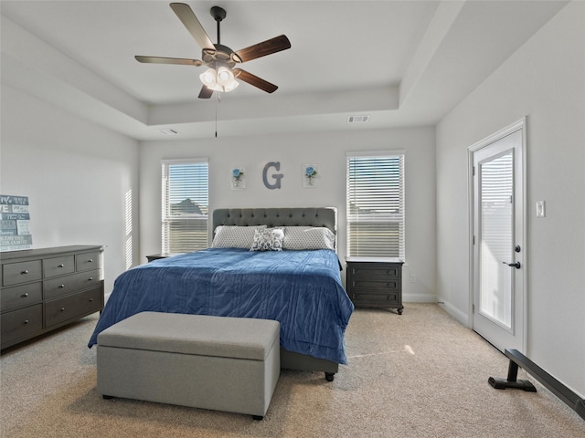 carpeted bedroom with a tray ceiling, visible vents, ceiling fan, and baseboards