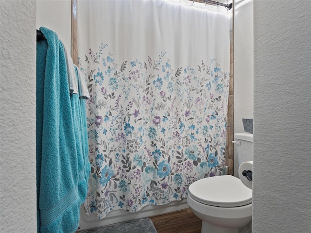 bathroom featuring toilet, shower / bathtub combination with curtain, wood finished floors, and a textured wall